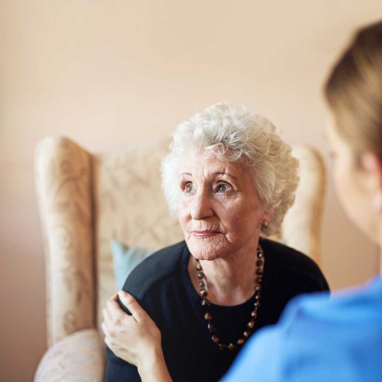 Two older adults smiling and having a conversation in a bright, comfortable common area.