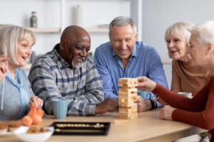 Volunteer and older resident play a card game together in a bright assisted living activity room.